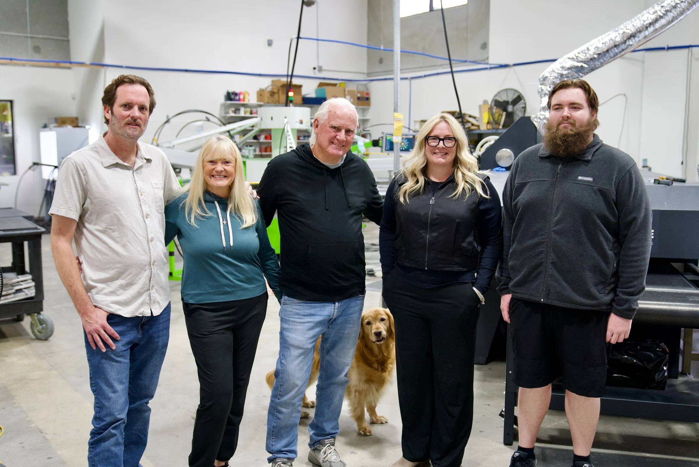 The Lamb Screen Printing family and their golden retriever standing in front of the shop's press