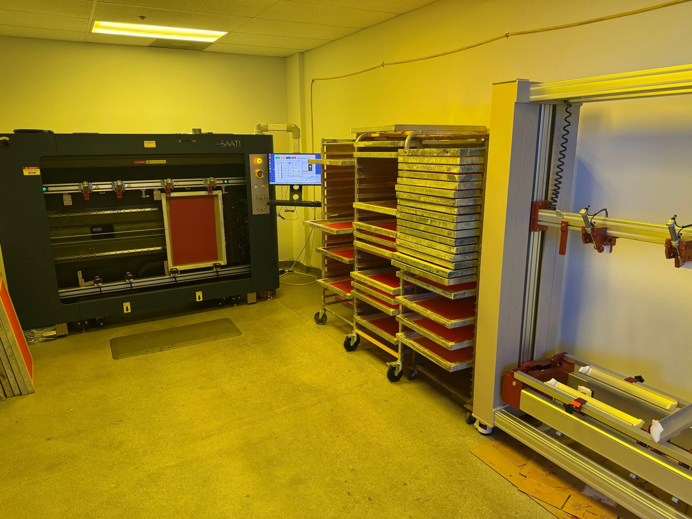 The shop's darkroom, with an exposure unit and racks of screens under yellow safelight