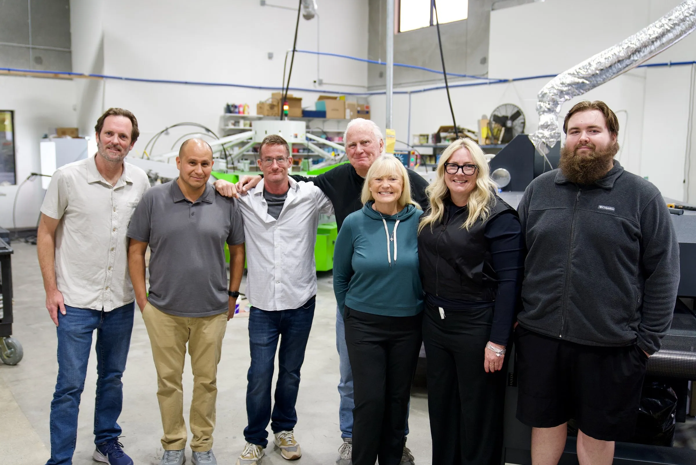 The whole Lamb Screen Printing crew standing in front of the press