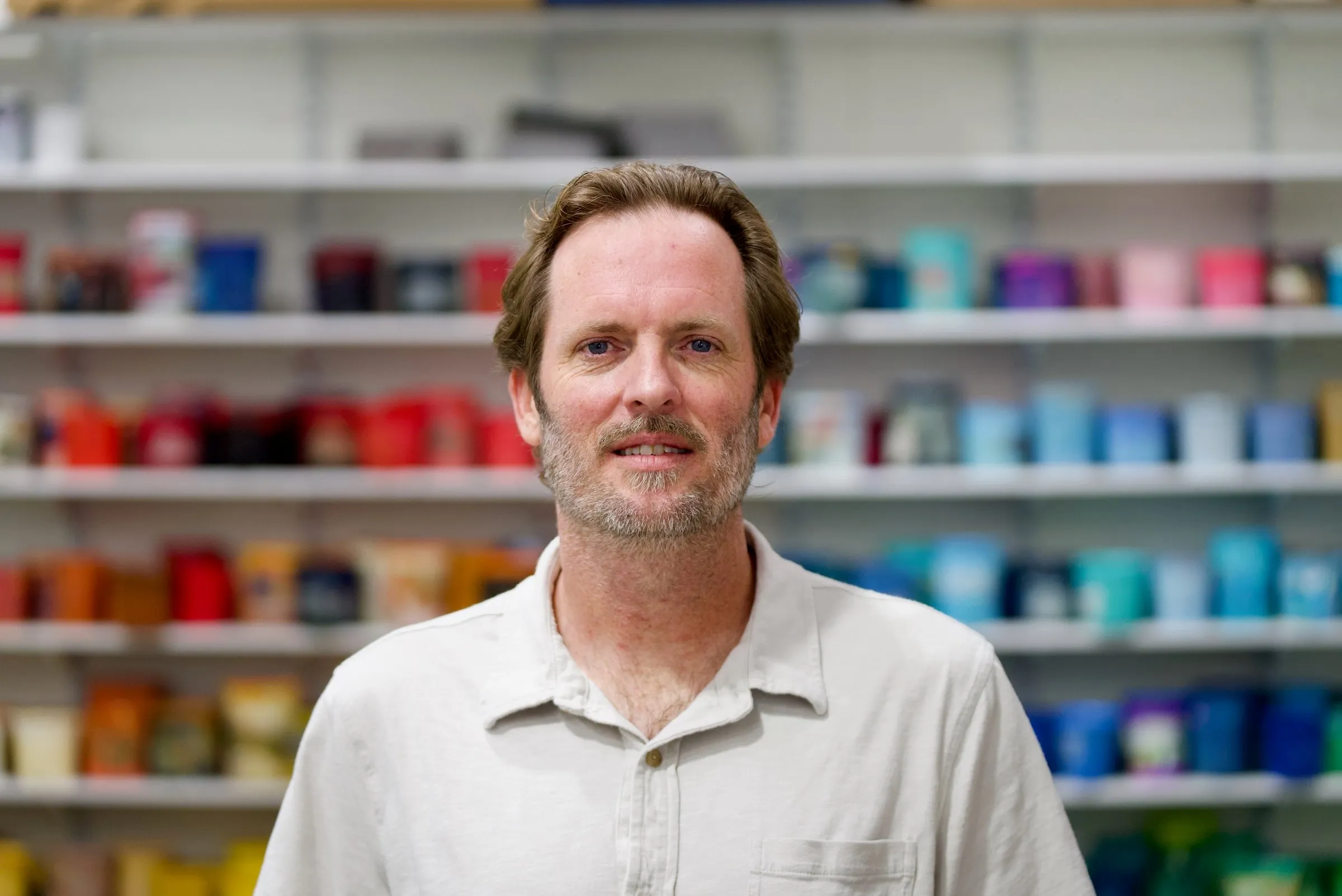 A member of the Lamb Screen Printing team in a light button-up shirt, in front of the shop's ink wall