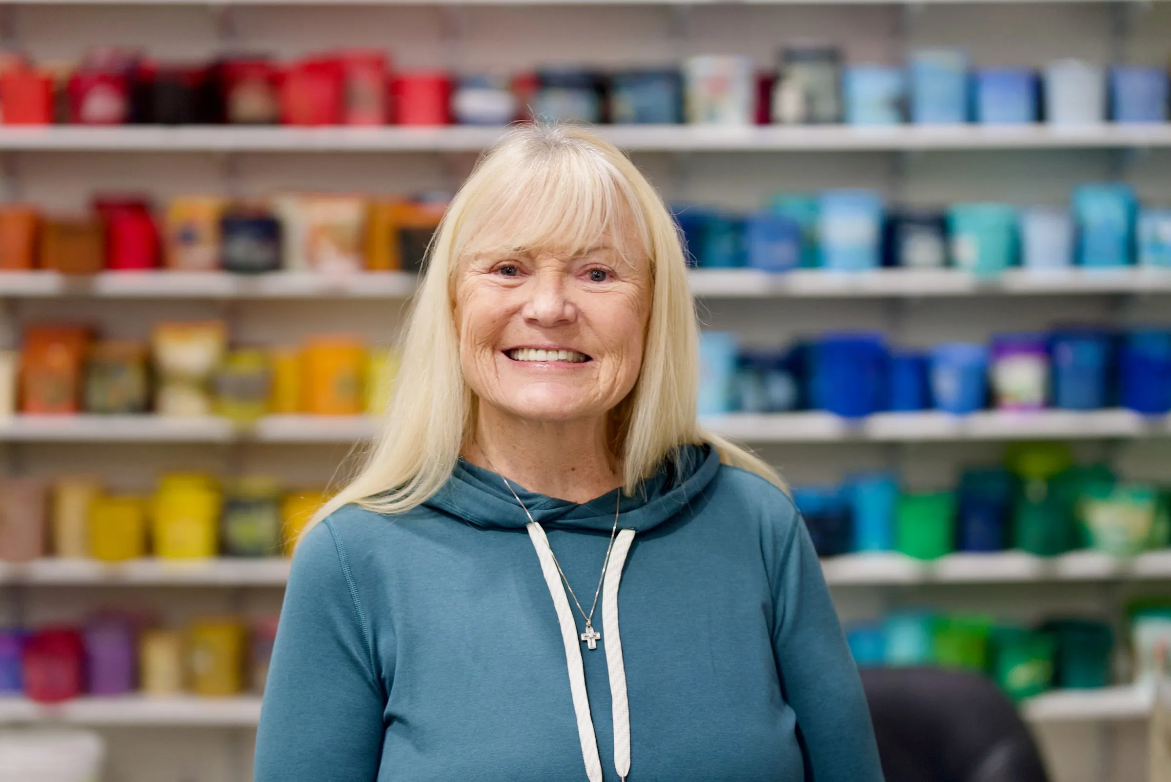 A member of the Lamb Screen Printing team in a teal hoodie, smiling in front of the shop's ink wall