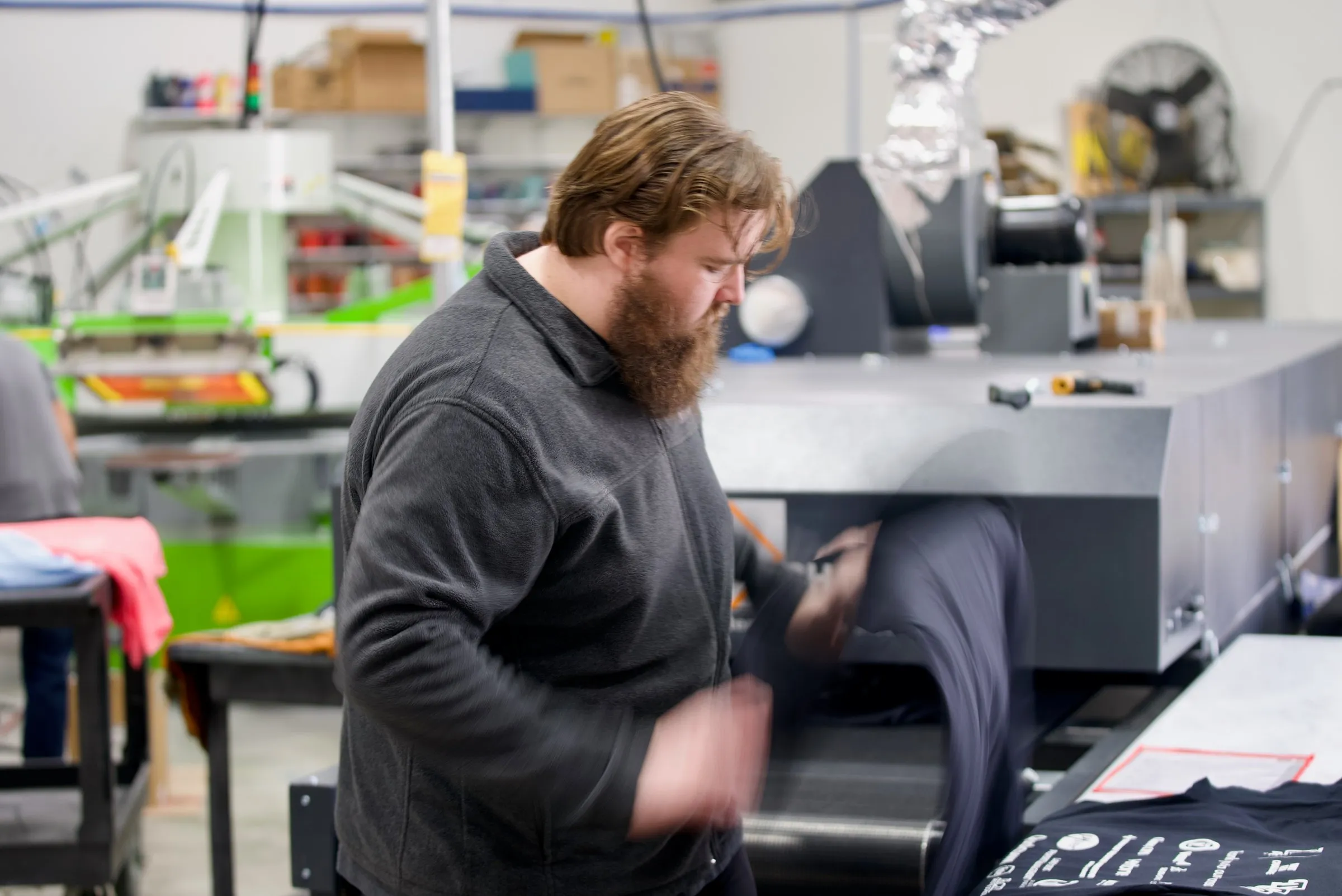 A printer catches freshly printed navy shirts as they come off the dryer belt