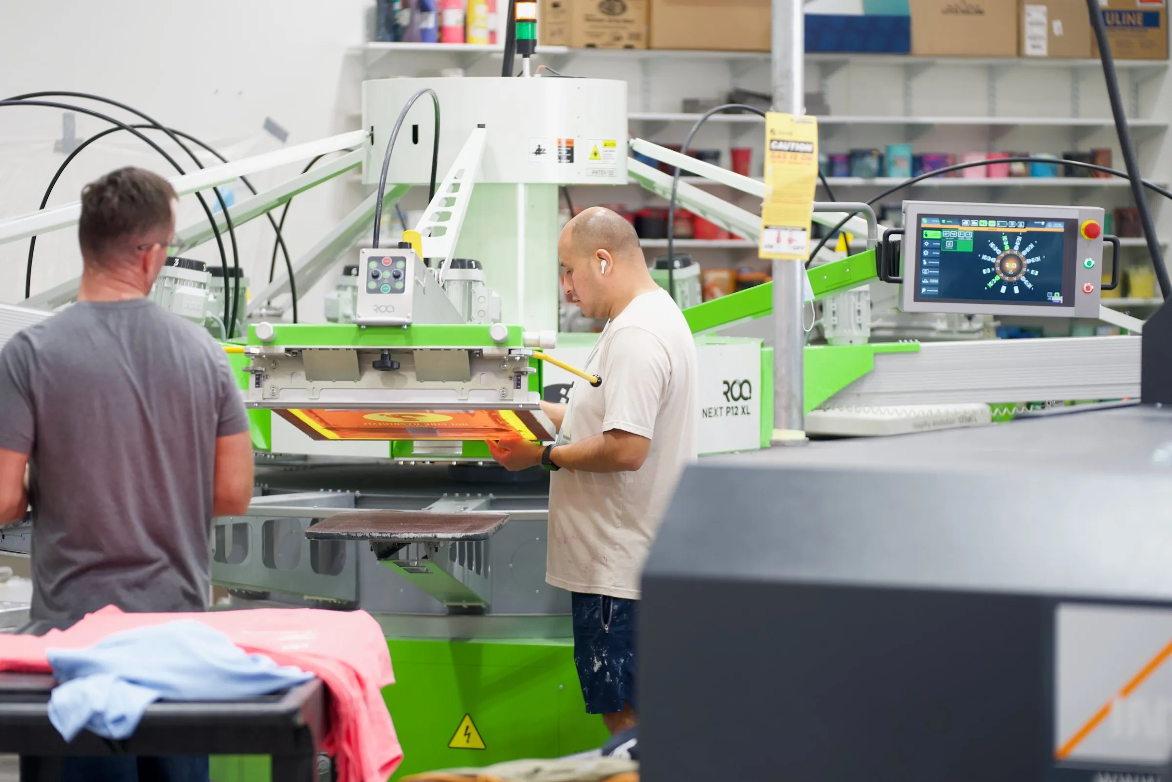 A printer lines up a screen on the automatic press while a coworker works at the next station