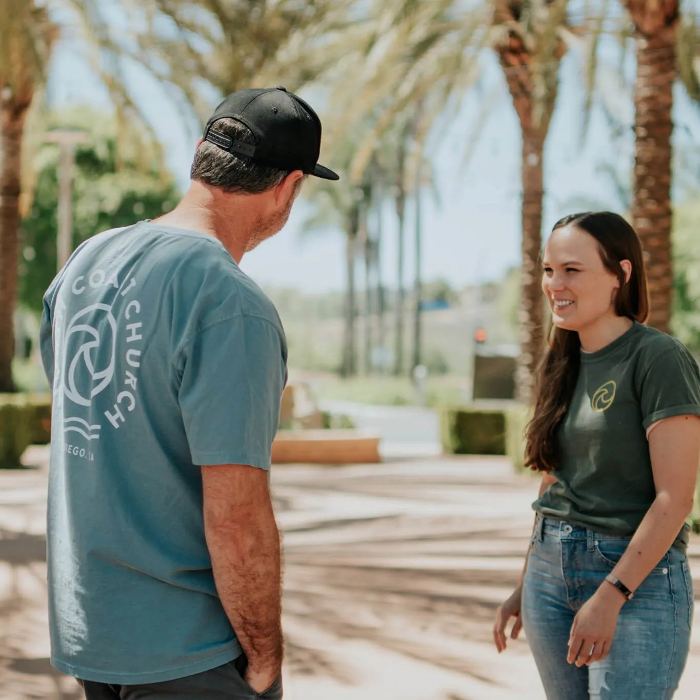 Two people talking outdoors, one wearing a church tee with a large back print