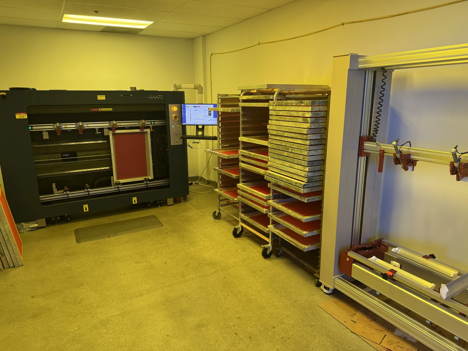 Our laser imager with a screen loaded, beside racks of coated screens in the yellow-lit screen room