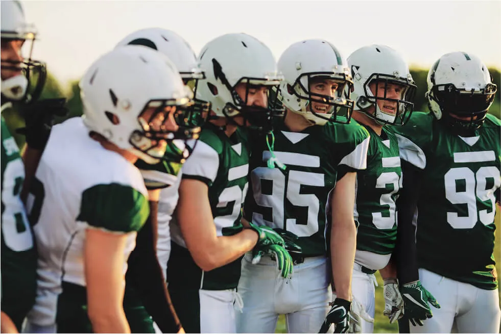 A team of american football players in green and white uniforms gathering on the field.