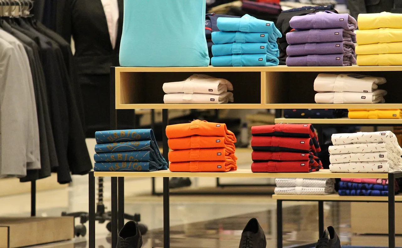 Neatly folded colorful shirts on display shelves in a retail clothing store.